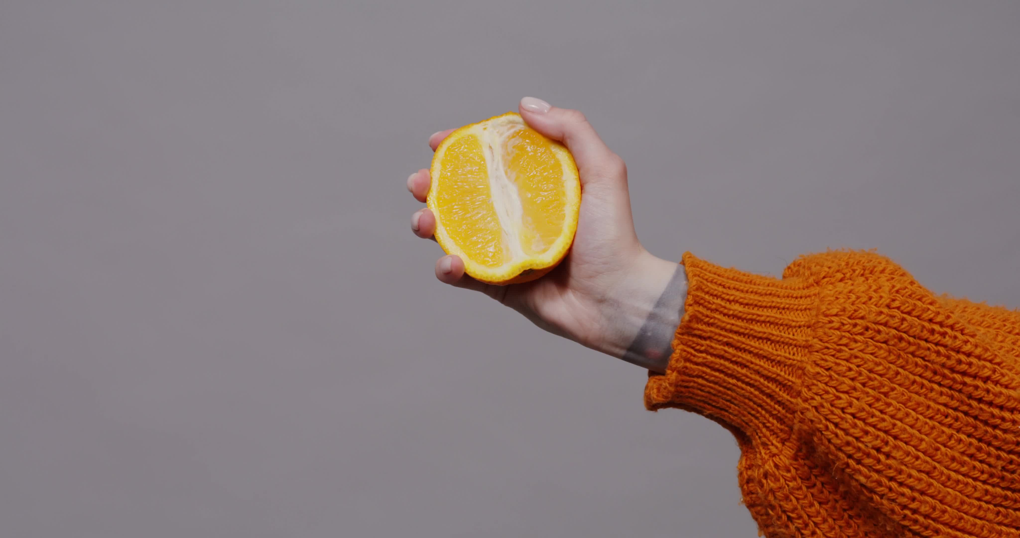 Holding a fresh orange half with a textured sweater in a neutral setting
