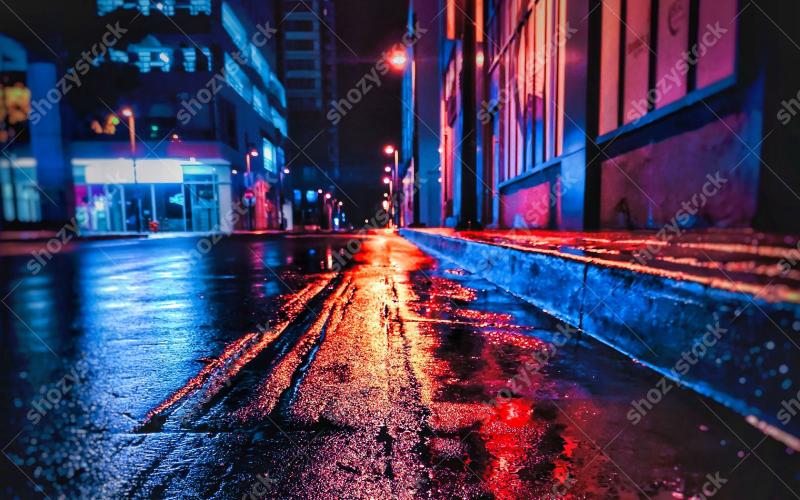 Urban street scene at night with vibrant reflections on wet pavement and ambient city lights